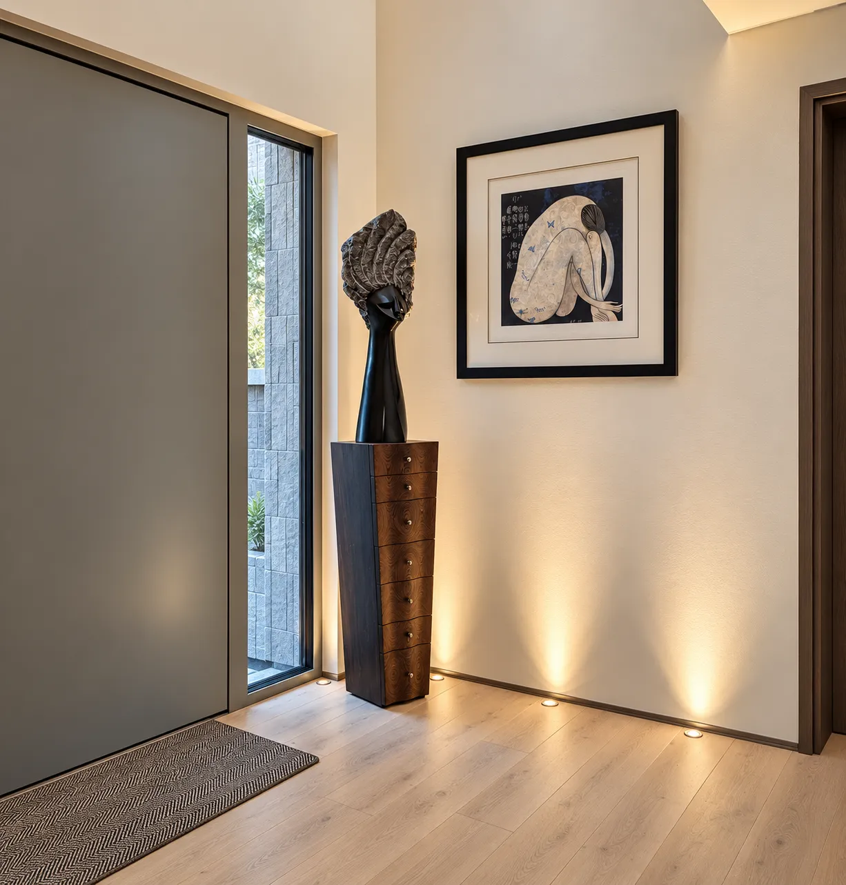 Entrance hall with a sculpture and artwork lit by recessed floor uplights